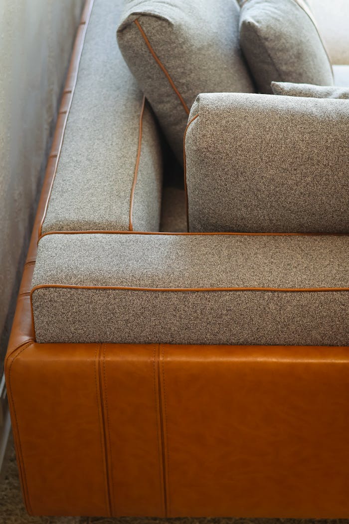 Stylish corner of a brown leather and gray fabric sofa with detailed stitching.