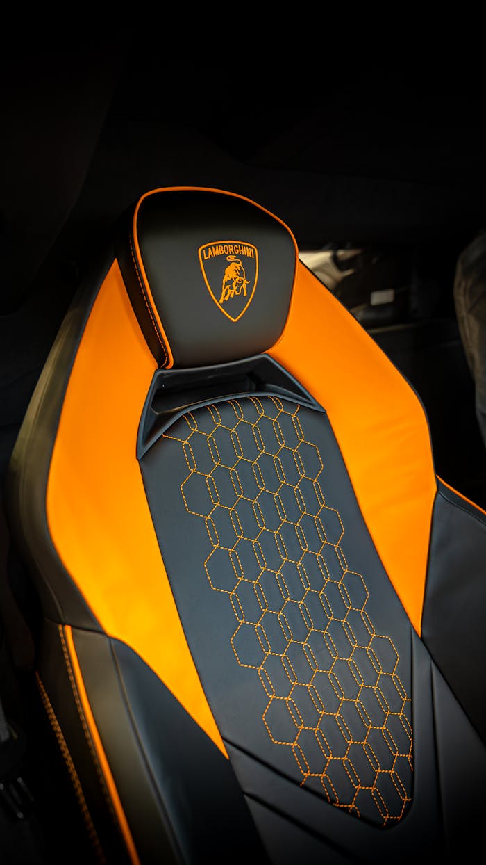 Close-up of a luxury sports car leather seat with orange accents and hexagonal stitching.