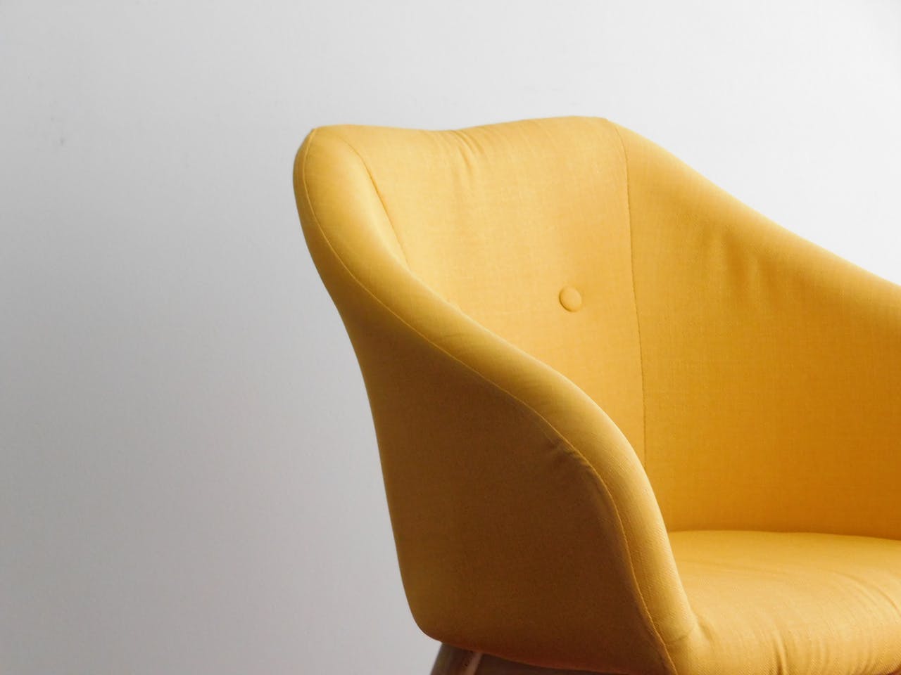 A bright yellow armchair stands against a white minimalist wall, showcasing modern design elegance.